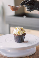 The girl sprinkles cocoa on the cupcakes through a sieve