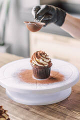 The girl sprinkles cocoa on the cupcakes through a sieve