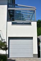 Moderne Einbau-Garage mit Automatik-Rolltor und darüber angeordneter Dachterrasse/Wintergarten, angebaut an ein modernes Einfamilienhaus