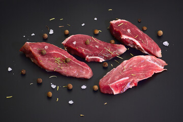 Slices of fresh raw beef steak with spices on black background. Top view flat lay with copy space