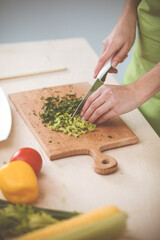 Unknown young woman slicing greens for a delicious fresh vegetarian salad while standing at the kitchen desk, just hands, close-up. Cooking concept
