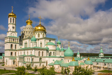Fototapeta na wymiar Istra, Moscow REGION, RUSSIA-AUGUST, 22, 2021: a beautiful architectural ensemble of white stone churches with golden domes in New Jerusalem on a sunny summer day against a bright blue sky with clouds