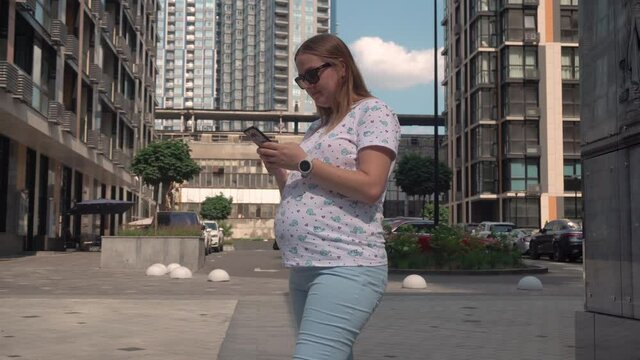 pregnant girl writes message phone against background industrial houses, straightens hair