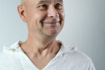 close-up face of a middle-aged man, a senior in white looks, smiles, the concept of emotions of the...