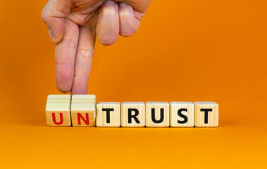 Untrust or trust symbol. Businessman turns wooden cubes, changes words 'untrust' to 'trust'. Beautiful orange table, orange background. Business and untrust or trust concept, copy space.