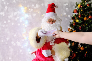 elderly santa claus with a white beard congratulates children and adults, holds banknotes in his hand, gives them, concept of christmas, holiday discounts, shopping, gifts