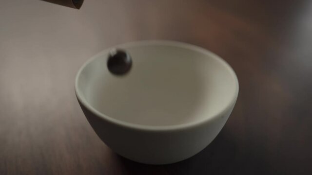 Slow motion chocolate covered hazelnuts pour into white bowl on walnut table