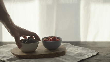 man put fresh strawberries and blueberries in bowls on olive wood board