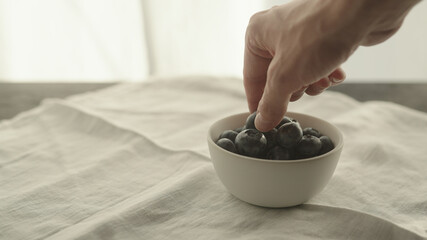 Fototapeta na wymiar man put fresh blueberries in white bowl on linen napkin