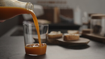 pour pumpkin juice into tumbler glass on concrete countertop