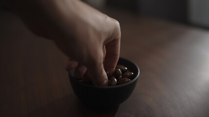 man hand take chocolate covered pistachios from black bowl on walnut table