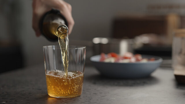 man pour amber drink in tumbler glass on concrete countertop