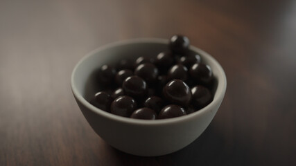 chocolate covered hazelnuts from white bowl on walnut table