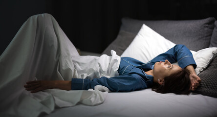 Thoughtful mature woman in blue pajamas lying in bed and looking on ceiling at night. Caucasian brunette suffering from insomnia at home. Life problems.