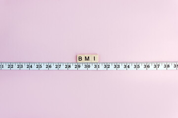 White measuring tape and word BMI on wooden blocks on pastel background. Control concept body mass index. Copy space.