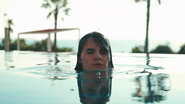 Young 30s brunette woman in swimsuit emerges from the swimming pool water touch hair enjoy summer holidays in tropical tourist resort, close up. Vacation, travel concept