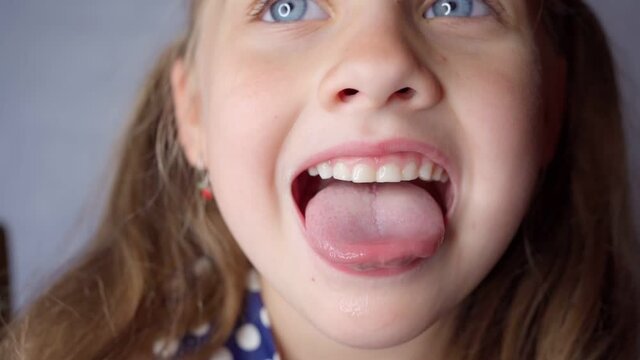 girl opens her mouth wide and pulls out long tongue. child shows his teeth soft palate and mouth to dentist. mouth is wide open, tongue is stuck out as far as possible, with clear view of tongue