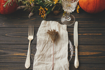 Thanksgiving dinner rustic table setting. Modern plate with vintage cutlery, linen napkin, herb on...