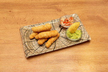Similar wooden log plate with a portion of tequeños stuffed with fresh cheese garnished with guacamole and pico de gallo