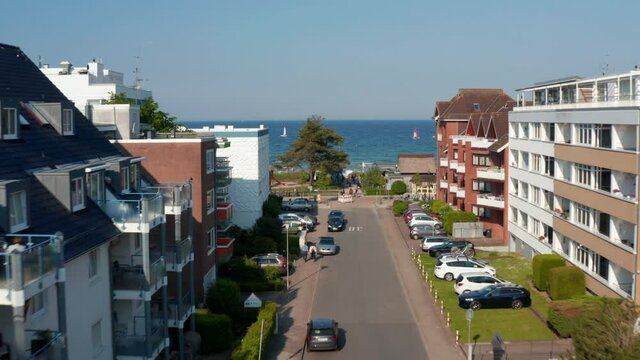 Aerial view flying between building street facing Baltic clear blue sea water in Scharbeutz, Germany, dolly in, day