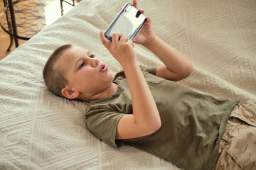Young boy lying on the bed and playing smartphone. Internet communication, modern technologies and people concept.