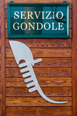 Vertical shot of gondola service sign and logo on the wooden background in Venice, Italy © Simone Padovani/Wirestock