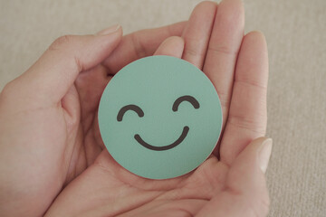 Hand holding green happy smile face paper cut, mental health assessment, child positive wellness,...