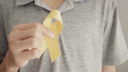 Teen boy hand holding yellow gold ribbon, Sarcoma Awareness, Bone cancer, childhood cancer...