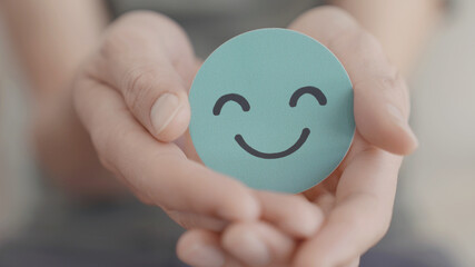 Hand holding green happy smile face paper cut, mental health assessment, child positive wellness, world mental health day, compliment  day, mindful concept - 452393669