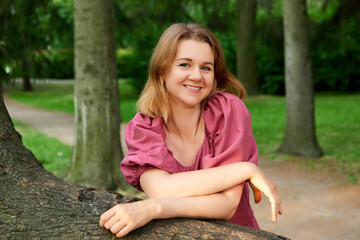 Happy woman stands near tree in park in summer.