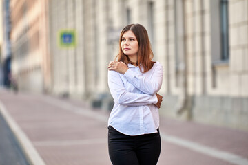 Woman with brown hair in shirt stands on street.