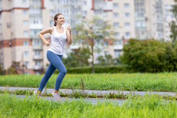 Smiling woman in leggins runs in public park in morning.