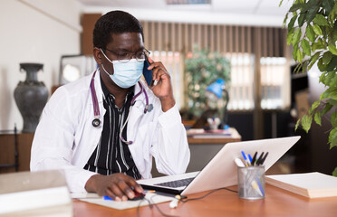 Fototapeta na wymiar Doctor in protective mask working in medical office using laptop computer