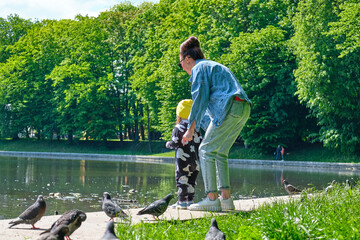 Mom and daughter are feeding bread crumbs to pigeons on the city pond.