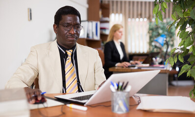 Fototapeta na wymiar Focused african american businessman works in the office at an computer while sitting at workdesk