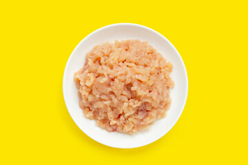 Minced meat of chicken fillet in white plate on yellow background.