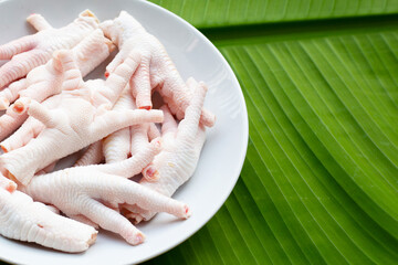 Raw chicken feet in white plate on banana leaf