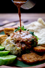 Dripping pecel on top of bean sprouts, spinach, and rice with tempeh garnish and cucumber slices. Pecel is indonesian traditional food from east java