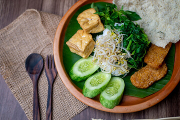 white rice topped with tofu, tempeh, vegetables, crackers, and sliced cucumber on a wooden table decorated with cutlery