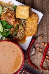 a bowl of sambal pecel juxtaposed with vegetables, tempeh and fried tofu with chili and peanut garnishes photographed on a wooden textured table