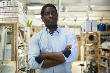 Confident african american man standing with arms crossed among shelves with goods in home decor accessories store