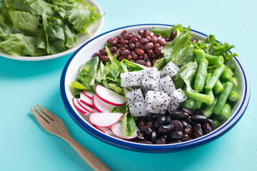 Healthy vegan salad vegetables with lettuce, corn salad, radish, kidney bean, azuki bean and green bean in a bowl on color background