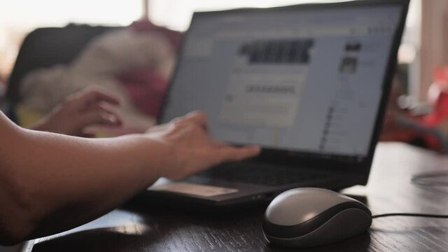 Young lady sitting on couch at home, using laptop, watching videos online, reading blogs, using social media. Lifestyle during covid-19 pandemic. Side shot.