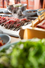 A view of sliced beef cooking on a table grill in the background, and a raw beef platter in the foreground, seen in a Korean BBQ restaurant.