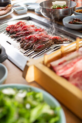 A view of cooked sliced beef in the background, and raw beef cuts in the foreground, seen in a Korean BBQ restaurant.