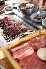 A view of cooked sliced beef in the background, and raw beef cuts in the foreground, seen in a Korean BBQ restaurant.