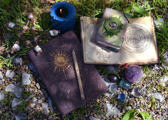 Still life with witch manuscripts and books, crystal and candles in the garden.