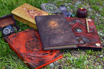Pile of witch grimoire book of magic spells and burning candle in the garden.