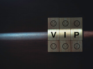 VIP words and boring faces emoticon on wooden blocks with the light on dark wood background with copy space. Privileges infringing on other people freedoms and civil liberties concept.