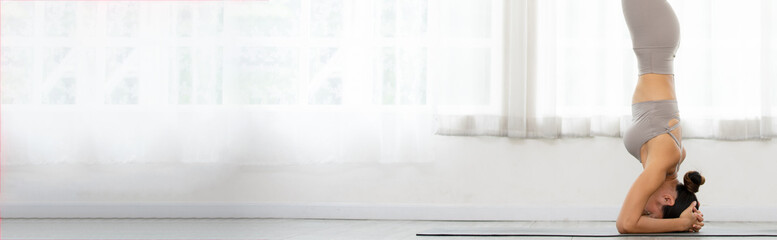Banner of Asian woman wearing sportwear doing Yoga exercise in front of windows,Yoga HandStand pose or Pincha Mayurasana,Calm of healthy young woman breathing and meditation yoga at home